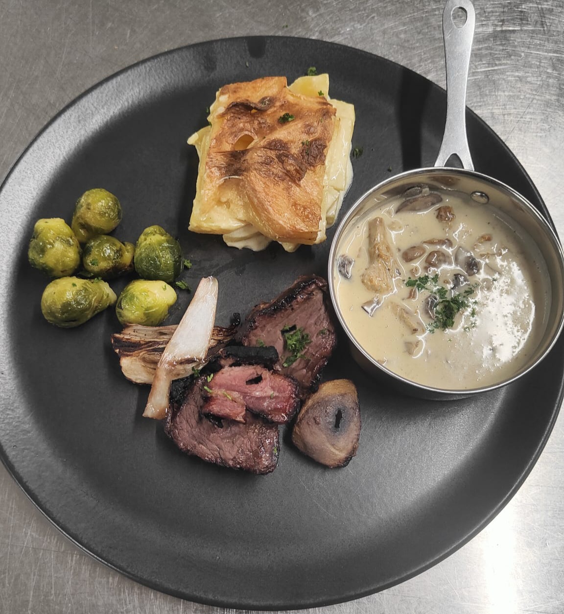 Assiette de viande, sauce crémeuse aux champignons, gratin de pommes de terre et choux de Bruxelles